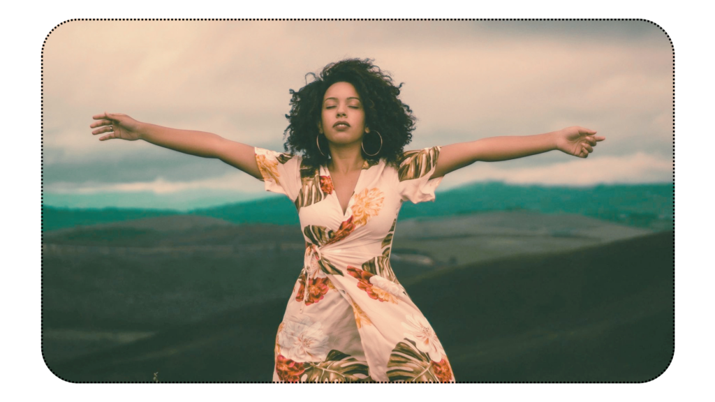 Woman, standing in a wide open space, arms open and eyes closed, looking like she is practicing letting go of the heaviness that has been holding her back.